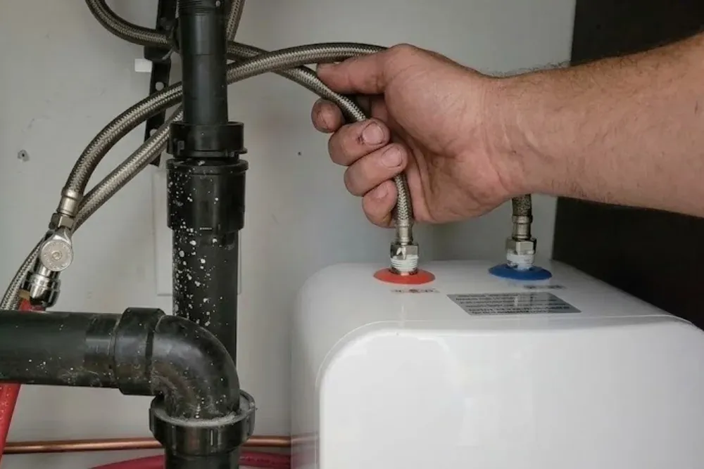 Hand connecting braided supply lines to the top of a water heater